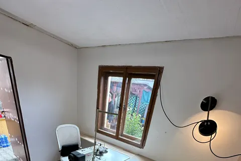 A small renovated room with wood-panelled walls, a window, wall lamps and a sewing machine on a white table.